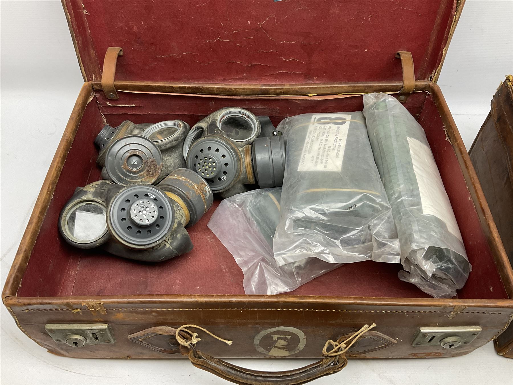 Early 20th century leather suitcase marked to the top 'Major P.M. Newton R.E. Crossways, Bridlington, East Yorkshire' 60 x 40cm; another similar leather suitcase marked W.D. to the lid; three post-WW2 respirators; and three unopened pairs of British Army N.B.C. (Nuclear Biological Chemical) No.1 Mk.III Trousers Protective (8)
