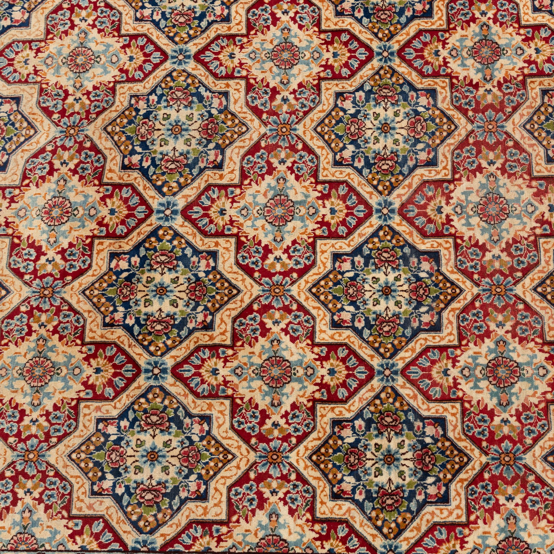 Central Persian Kirman carpet, the field arranged with alternating indigo star shaped and red cruciform compartments, each filled with rosettes, flowerheads and scrolling foliage, enclosed by a broad ivory palmette border and red floral guard bands