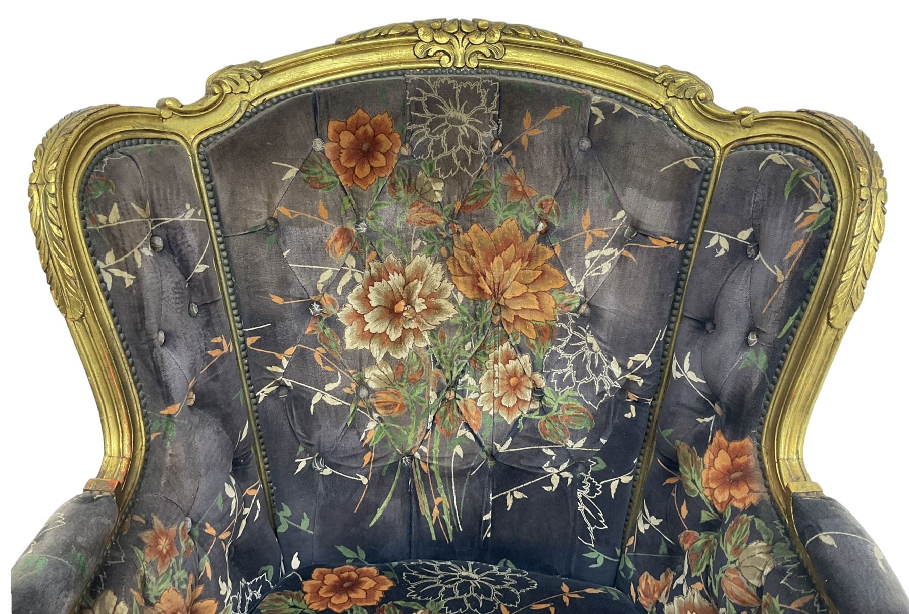Pair of Louis XVI design gilt framed wingback armchairs, cresting rail carved and moulded with foliate decoration and C-scrolls, upholstered in buttoned floral patterned mauve velvet with loose seat cushion, scallop carved apron over cabriole supports