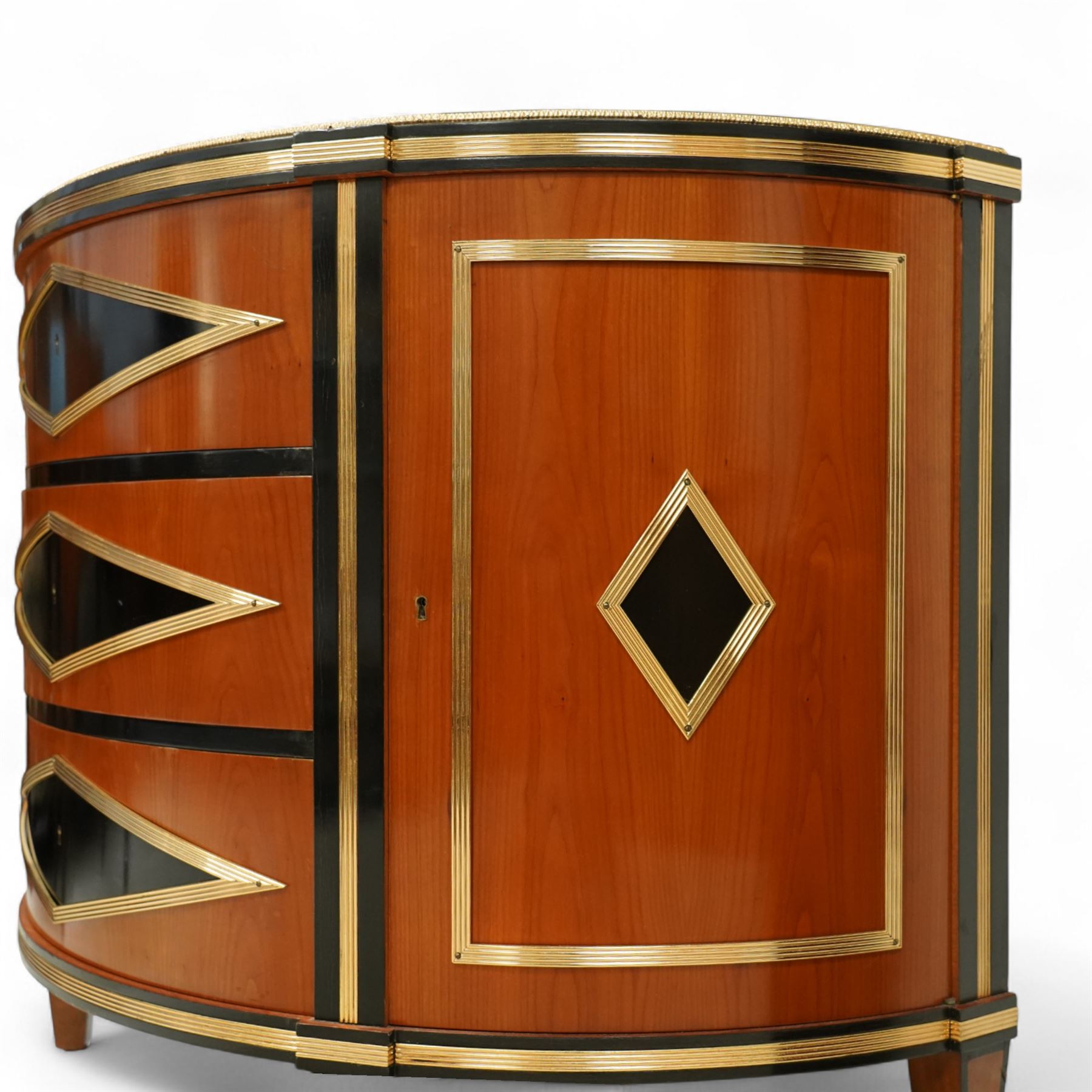 Colombo Mobili - Pair of Italian designer cherrywood art-deco inspired demi-lune commode cabinets, the shaped top with ebonised inlay and gilt brass repeating anthemion beading above a gilt brass reeded moulding, over three long drawers with gilt brass geometric panel mounts, flanked by cupboard doors with diamond motif, raised on tapering square supports 