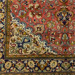 Central Persian Qom hand-knotted carpet, salmon pink ground, with a central dark navy shaped floral medallion with pendants, surrounded by dense scrolling foliate and floral motifs incorporating rosettes, palmettes and delicate vine work, enclosed by ivory spandrels and a dark navy border with repeating palmettes and meandering vines, flanked by narrow floral guard stripes, with cotton fringes