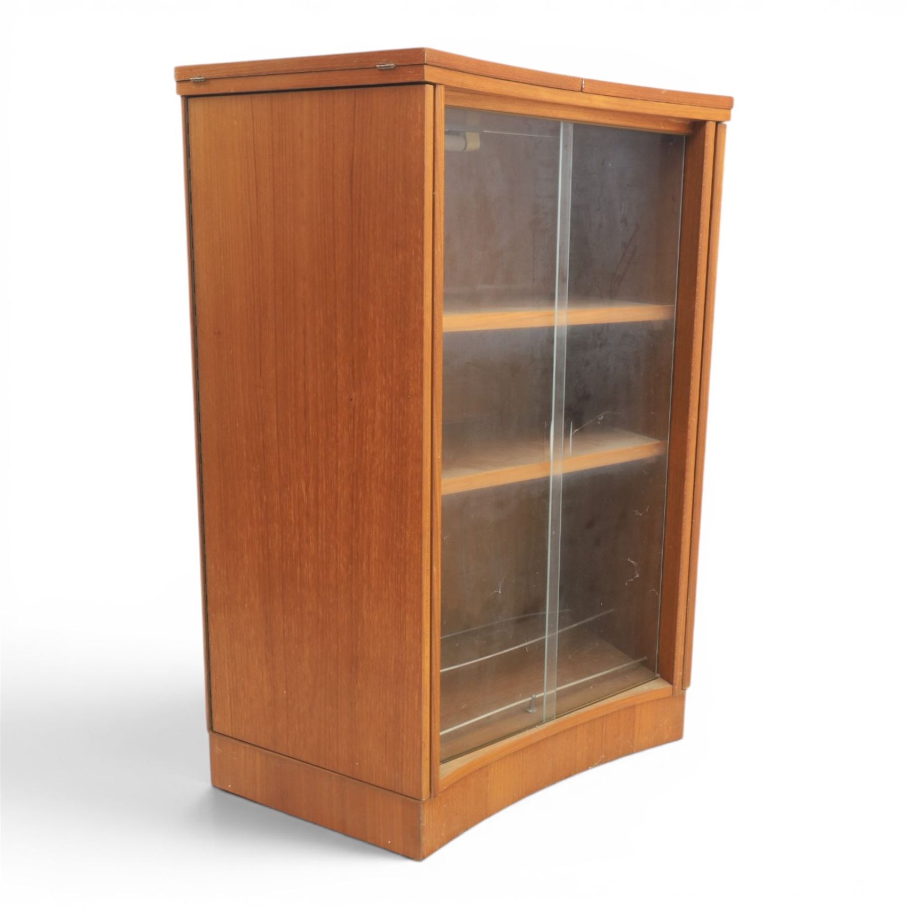 Turnidge of London - Mid 20th century teak drinks cabinet, shaped top with hinged fold-out side sections, twin doors with recessed handles enclosing fitted shelving and serving surfaces, sliding glass doors to the back, on a plinth base above castors