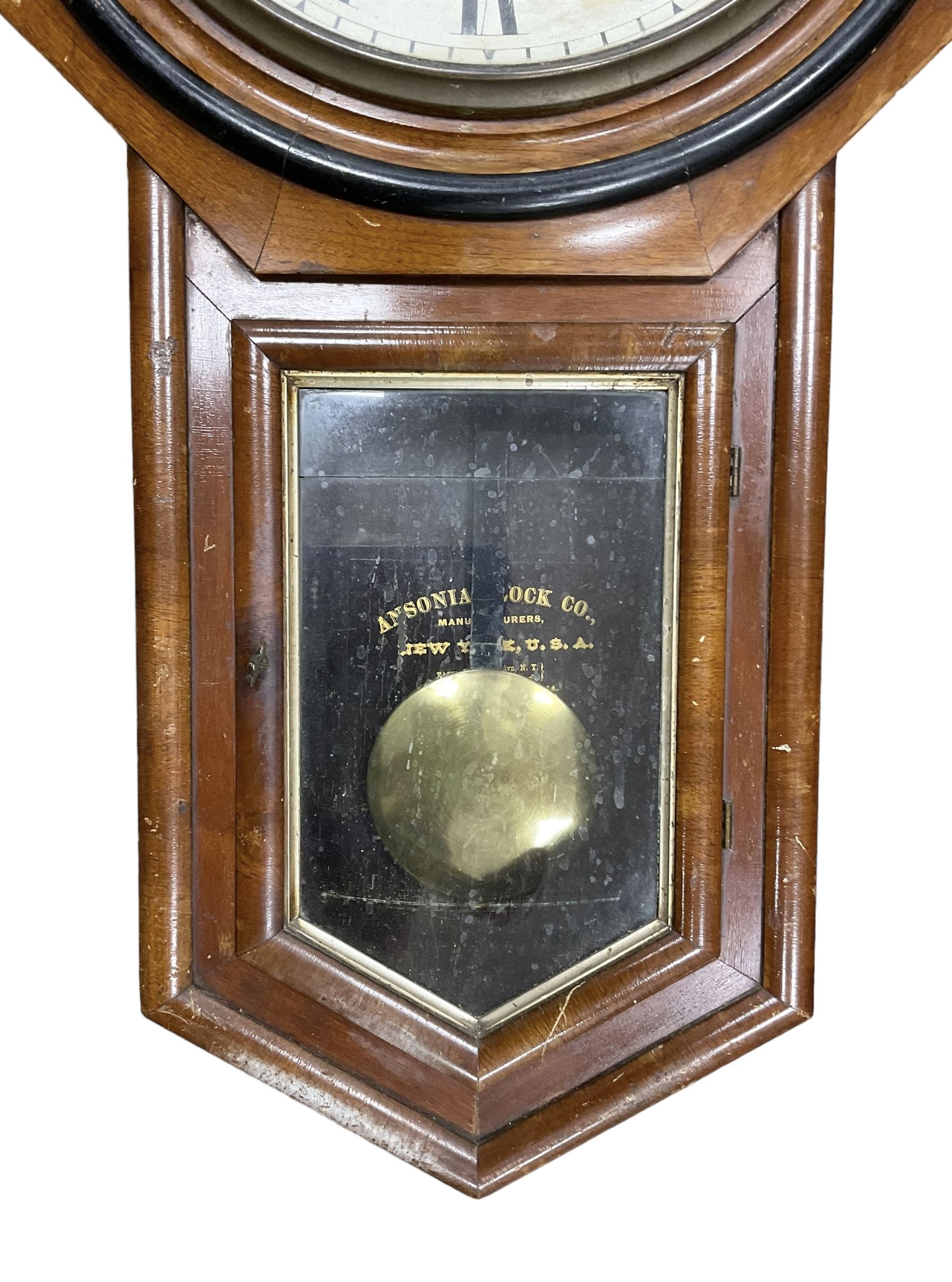 American - Late 19th century Ansonia 8-day wall clock, with a hexagonal wooden dial surround and circular spun bezel, glazed case door and visible pendulum,  two part dial with Roman numerals, minute track, spade hands and seconds dial, twin train spring driven movement striking the hours on a gong.