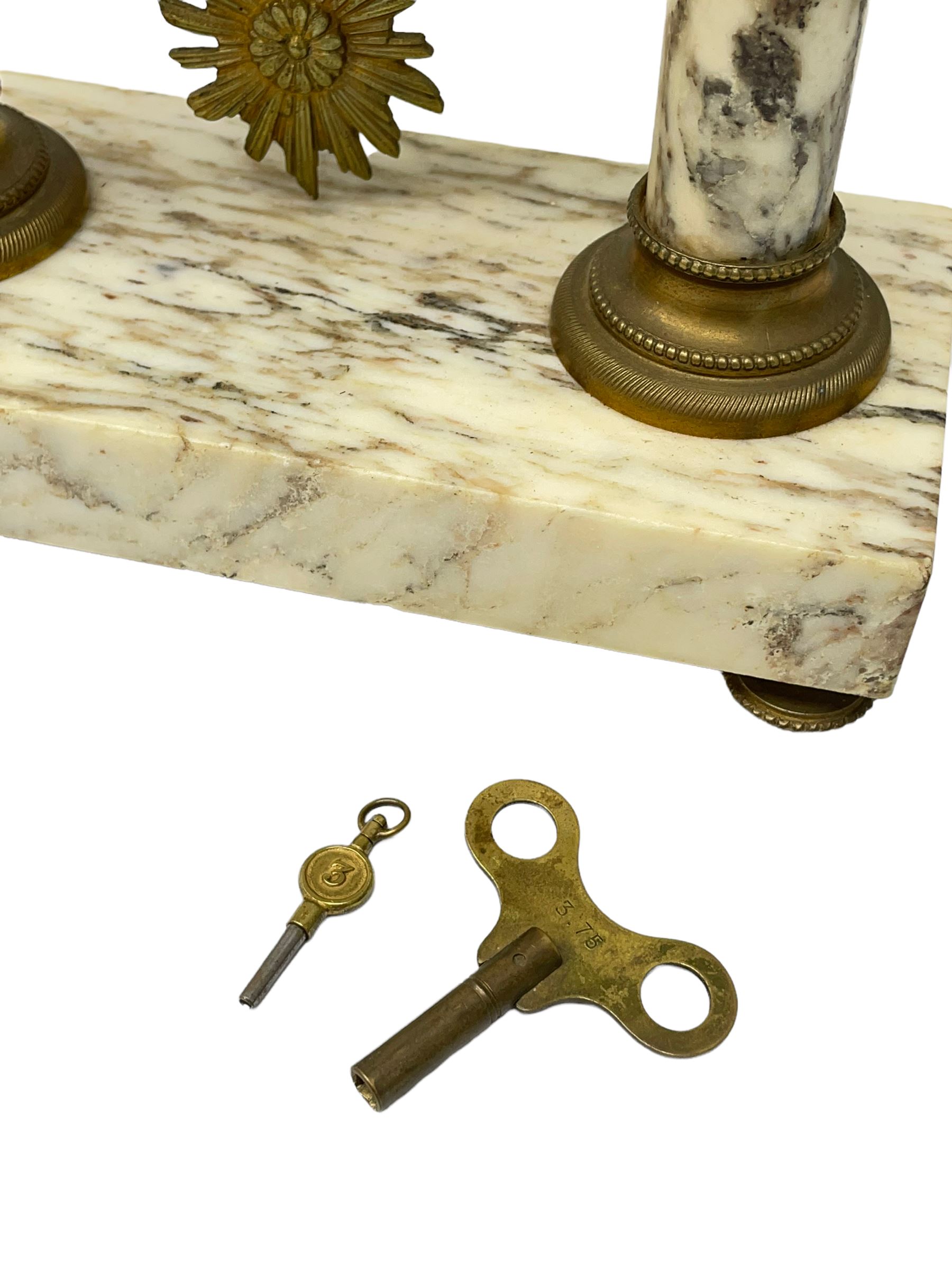 20th century French portico clock c1910 on a white veined marble base, gilt drum movement case supported between two marble columns with brass capitals and a suspended garland swag with a starburst pendulum beneath, enamel dial with Arabic numerals, floral decoration and Louis XV pierced gilt hands, convex glass and brass bezel, 8-day countwheel striking movement striking the hours and half hours on a bell. 




