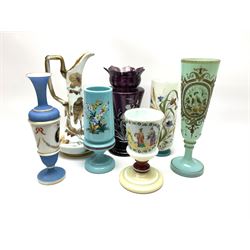 A group of mostly Victorian painted glass, to include a light blue opaque glass vase with funnel bowl upon a spreading circular foot, decorated with a bird, butterfly and flowers within a gilt frame surround, H31.5cm, a milk glass ewer decorated with a bird upon branch with flowering tendrils, H32.5cm, a Mary Gregory type amethyst glass vase, with castellated rim decorated in the typical manner with child amongst long grasses, H28cm, a milk glass goblet decorated with an Oriental style figural panel, H19cm, etc.