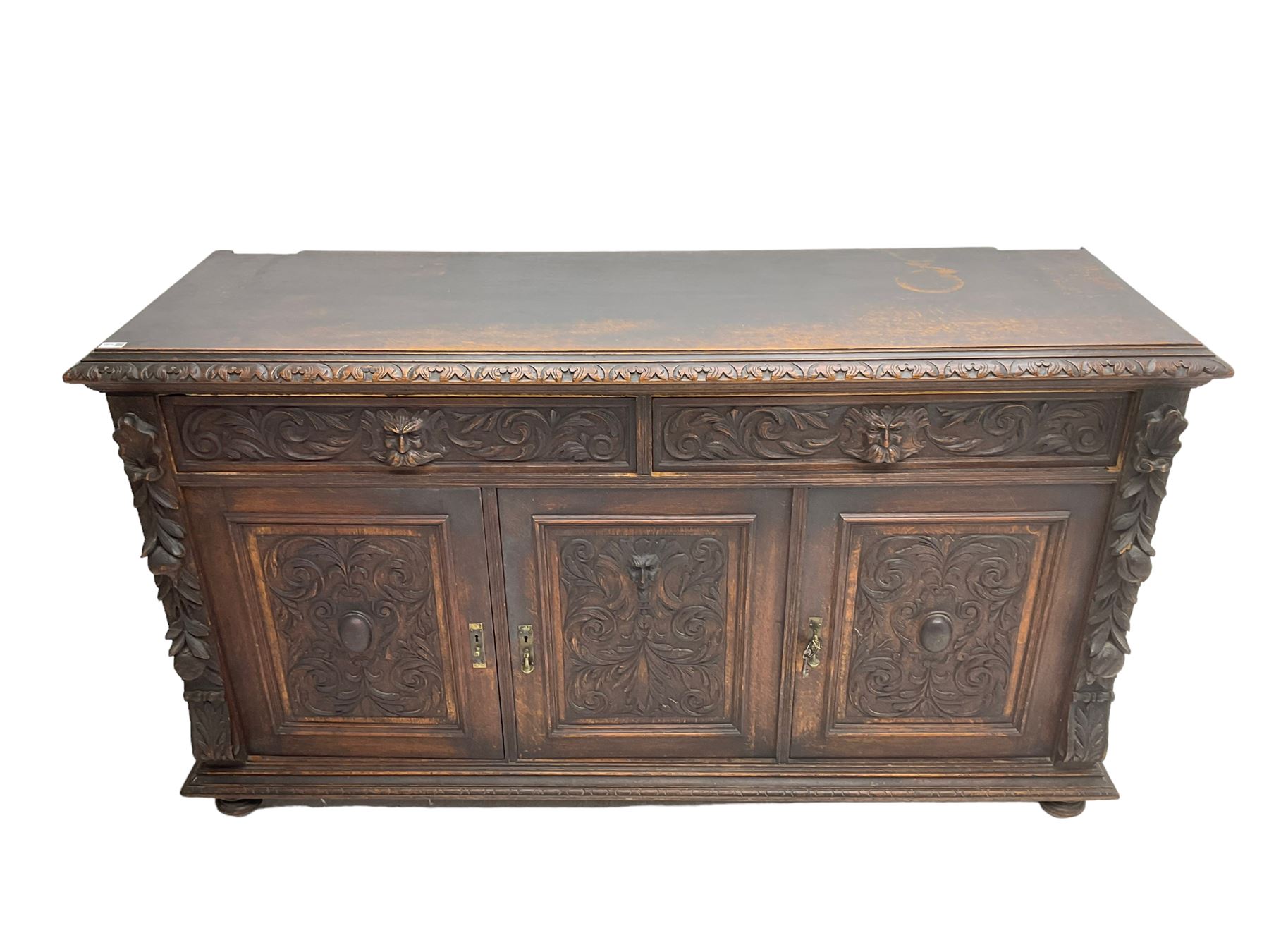 Victorian heavily carved oak sideboard, the moulded top carved with foliate decoration to the edge, fitted with two drawers and three cupboards, the drawer fronts carved with green man mask handles and scrolling foliage, the panelled doors carved with interlacing foliage, on turned compressed bun feet