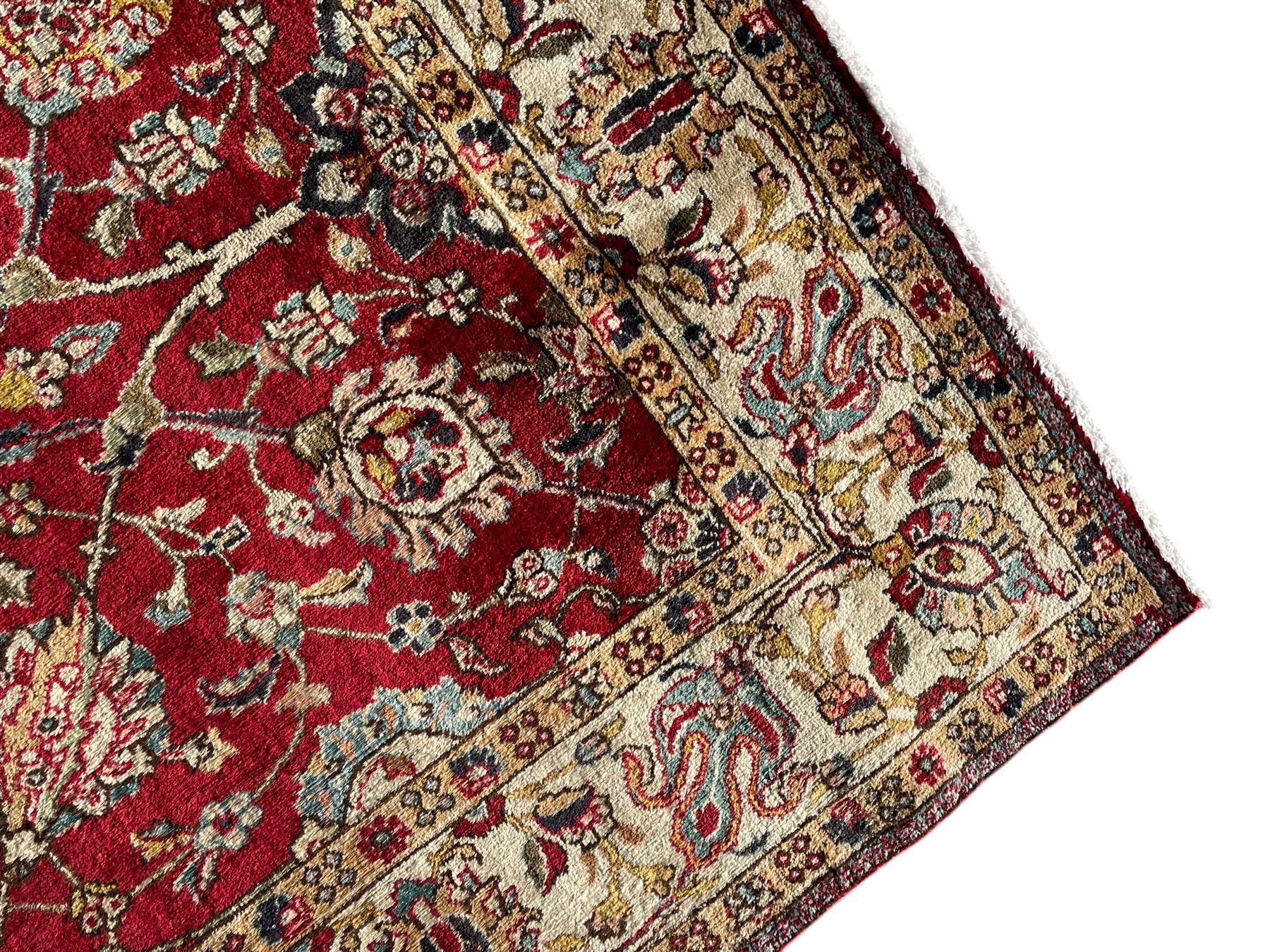 Persian Tabriz crimson ground rug, the field decorated with large palmette and stylised plant motifs connected by interlaced leafy branches, trailing border decorated with similar palmette motifs within floral pattern guard stripes, with signature panel 