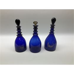 Three George III 'Bristol Blue' decanters, of mallet form with triple ring necks, two examples with remnants of gilt inscriptions 'Brandy' and 'Gin', two with pear shaped stoppers, the other with mother of pearl stopper inscribed 'Brandy', tallest H29cm