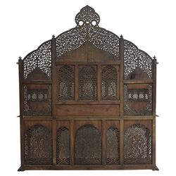 Late 19th century Indian Burmese carved and pierced hardwood and brass inlaid wall shelf, the shaped back profusely decorated with trailing and interlaced foliage, with projecting architectural structures, the central balcony with canopy top and five open windows with arched apertures on columns, two flanking five-sided balconies, the shelf supported by six foliate carved columns with pierced cusped pointed arches 