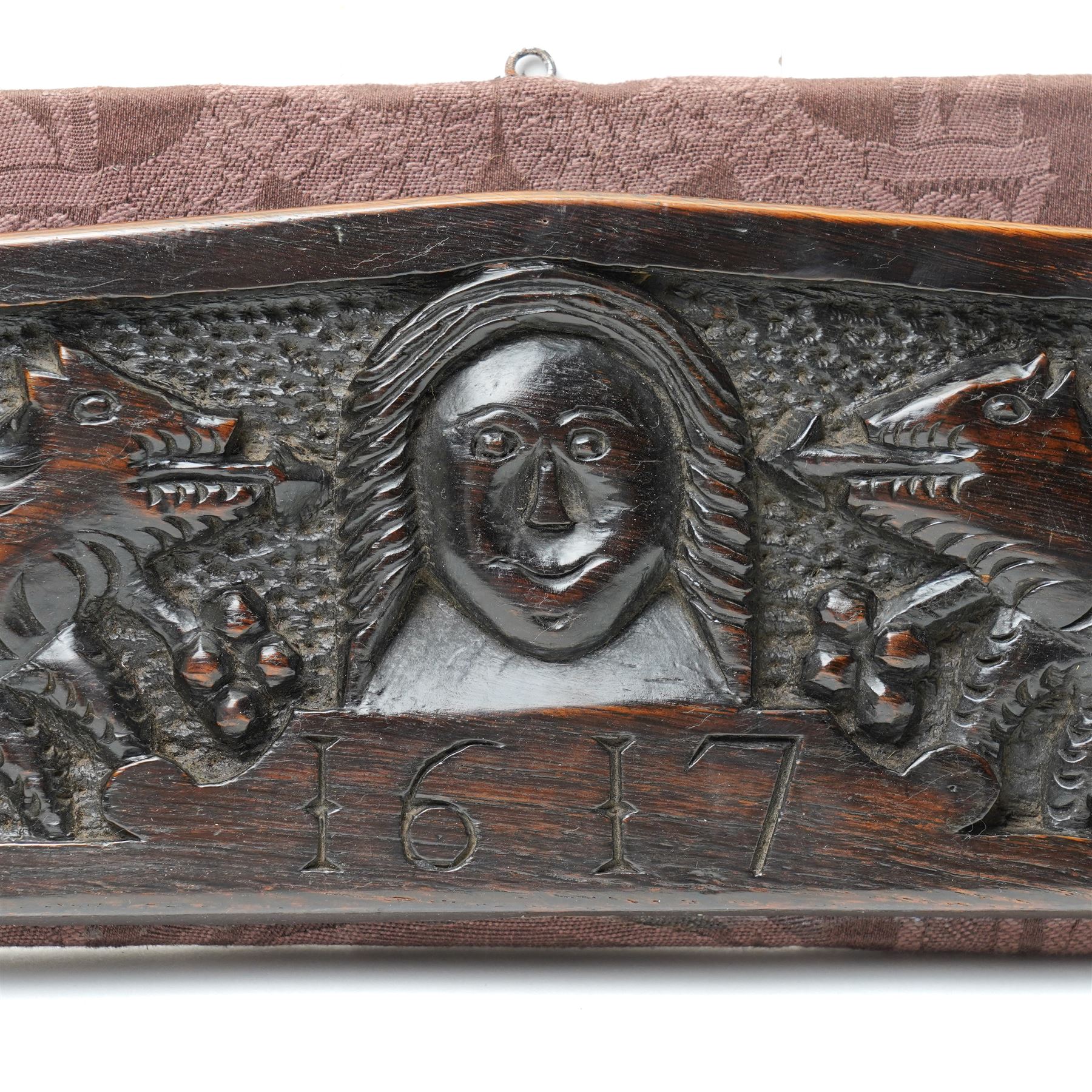 17th century walnut frieze, or pediment, carved with a smiling mans faced flanked my two creatures, incised date 1617, mounted on fabric panel, W52cm