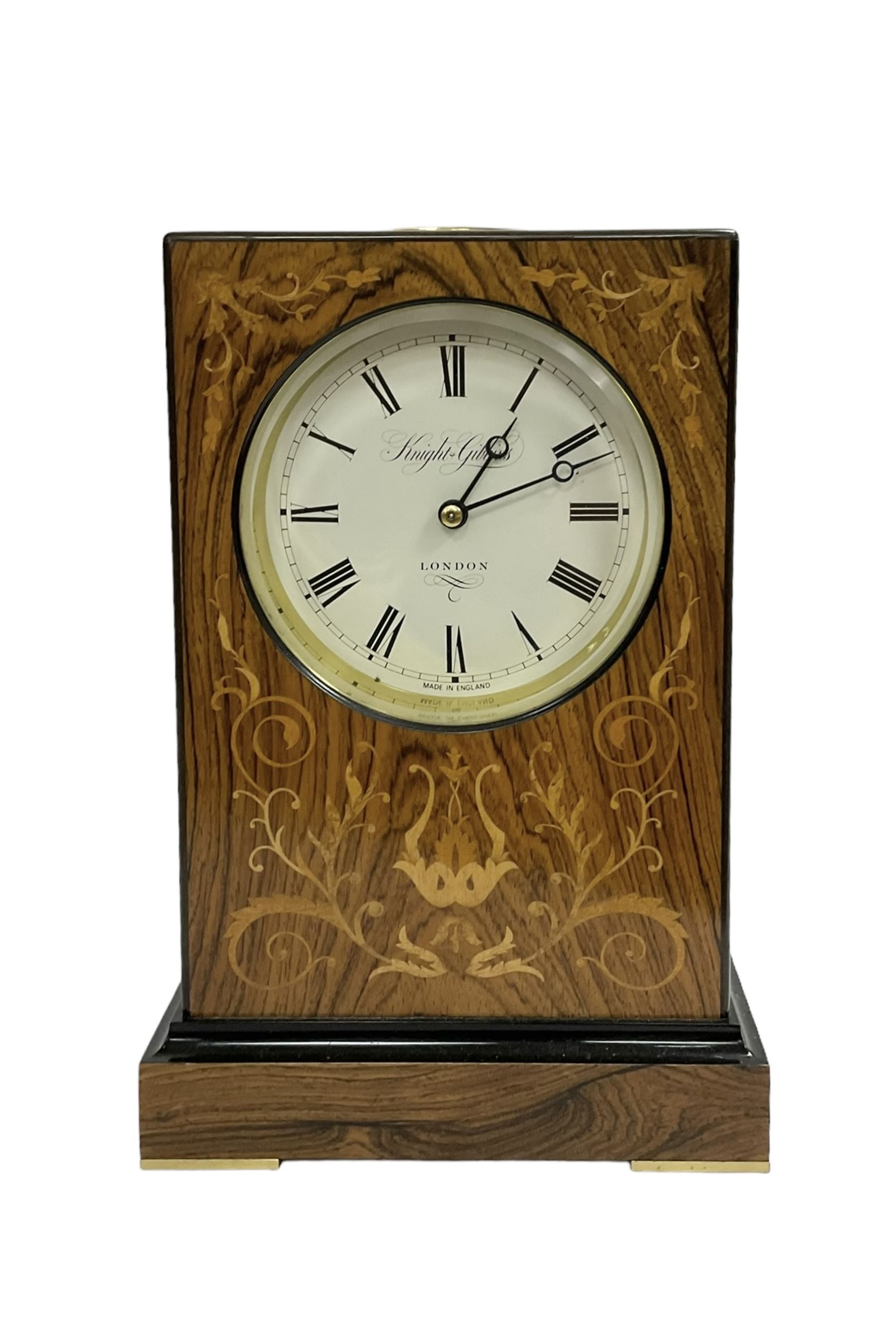 Knight & Gibbins London - 20th century 8-day marquetry inlaid mantle clock in rectangular case on a short plinth, glazed circular dial with Roman numerals and steel moon hands, two train striking movement with a floating balance escapement striking the hours and half hours on a bell, rear set and wound. With key.   