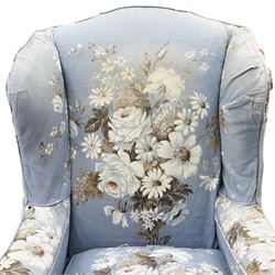 Pair of Queen Anne wingback armchairs, high back over out-swept arms, raised on ball-and-claw feet, upholstered in sky-blue ground floral chintz loose upholstery with pleated skirt and squab cushion