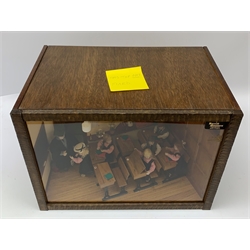 A 1/12th scale diorama of a school room interior, depicting pupils and teacher, the room furnished with panelled wall, desks, chalk board, globe, books and dunces hat, etc., H29cm L40cm D26cm.  
 
This model is based on a Victorian School Room in the museum in Armley, where the children and teachers would dress in period costume and attend lessons during the summer time.