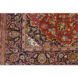 Central Persian Kashan hand-knotted rug, deep red field with central cusped ivory medallion with an all-over arrangement of scrolling floral vines, palmettes and flowering sprays within conforming spandrels, principal navy border with a continuous meandering vine of palmettes and stylized floral motifs, enclosed by multiple narrow guard borders, with cotton fringe ends 