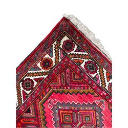 Persian Hamadan red ground rug, decorated with six stepped lozenge medallions, the guarded border with repeating stylised flower head decoration, with inscription to corner