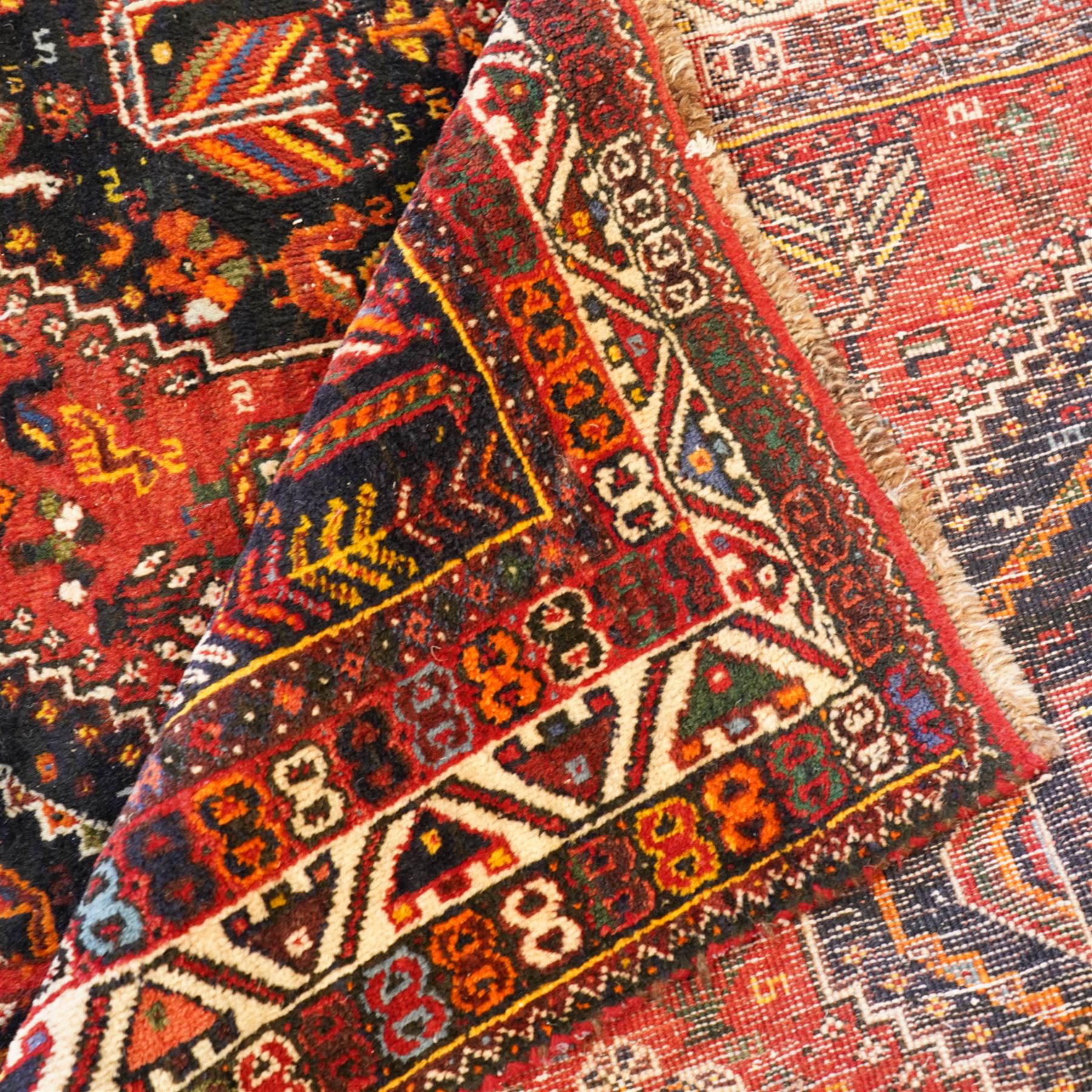 Persian Shiraz crimson ground rug, triple pole medallion surrounded by small stylised motifs depicting birds, animals and plants, within multiple band border each decorated with repeating patterns