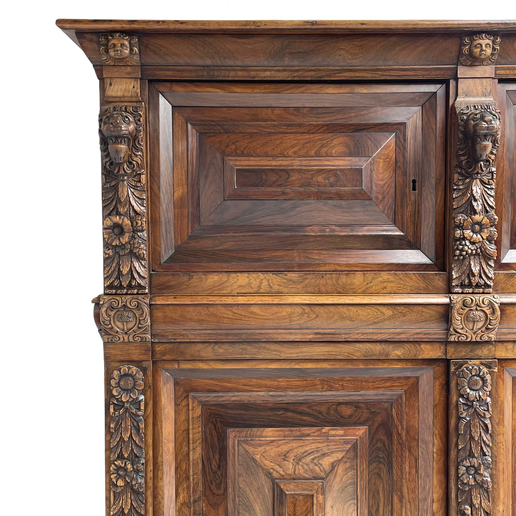 Late 17th century Flemish/Dutch rosewood and oak ‘Zeeuwse Kast’ or cupboard, projecting cornice carved with three putti masks, the uprights carved with lion masks over ribbons, flower heads and foliage, enclosed by four geometric panelled doors, lower central upright carved with flower head over foliate ribbon with bird among foliage, the escutcheon hidden by swivel berry carved cover, interior fitted with shelves, two drawers and shallow hinged cupboard, on two large turned and ebonised feet, circa 1680