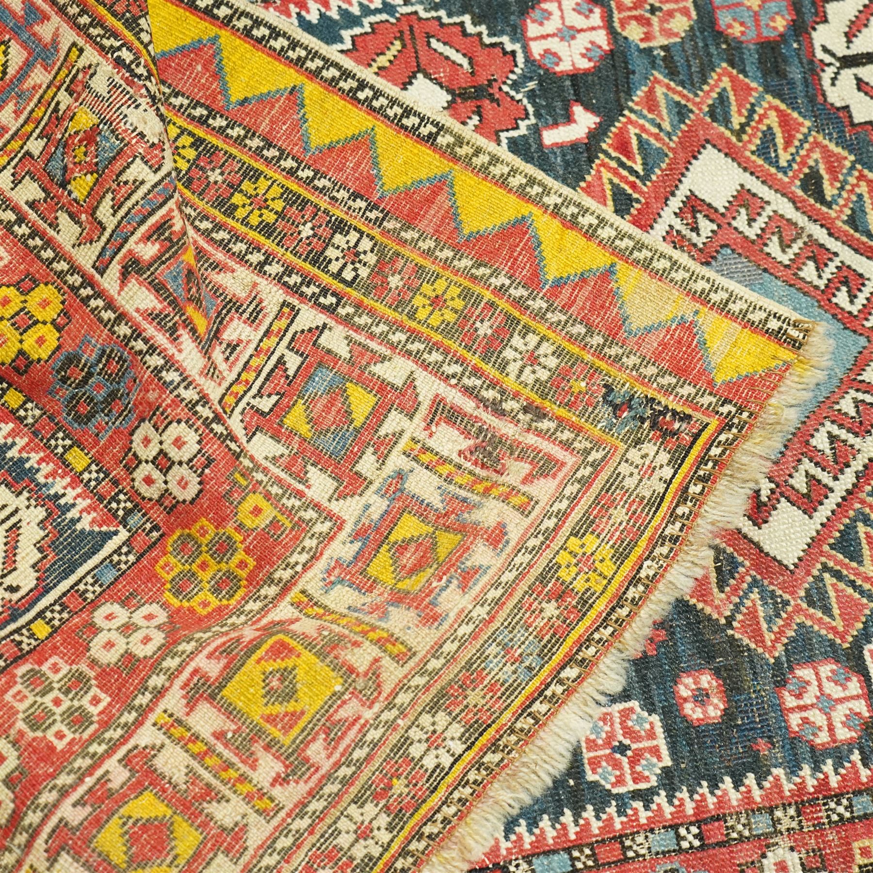 Vintage Caucasian Shirvan hand-knotted rug, indigo field with an arrangement of geometric diamond medallions and stylized tribal motifs within multiple patterned borders, with fringe ends 