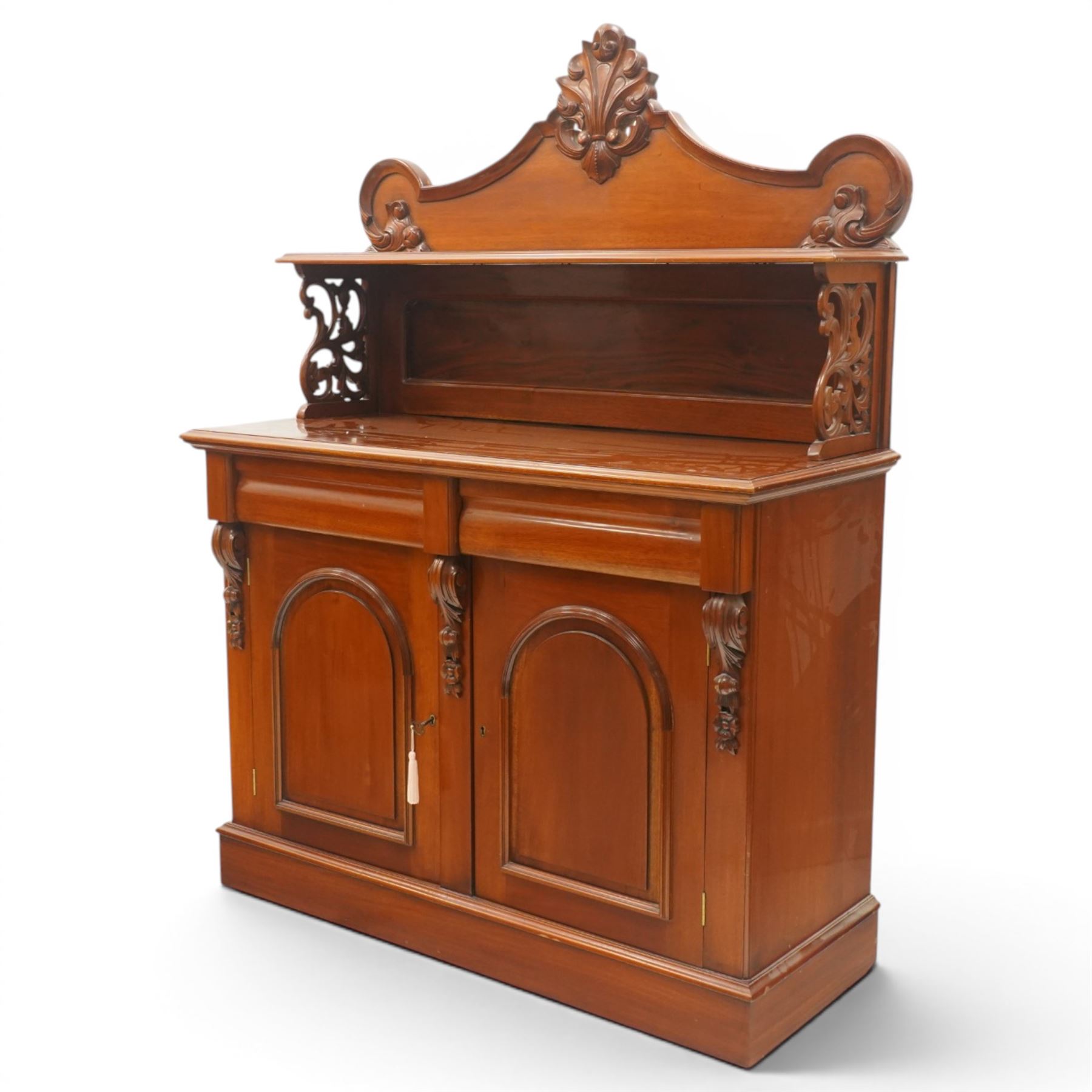 Victorian mahogany chiffonier, the superstructure with shaped back and pierced side supports above a shelf, moulded top over twin arched panel doors enclosing cupboard interior, with carved scroll brackets, on plinth base