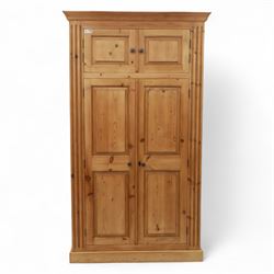 Modern stripped pine double wardrobe, with stepped cornice over upper cupboard doors and two full-height fielded panel doors, fluted stile detailing, ebonised knob handles, and plinth base