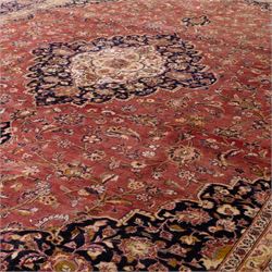 Large Central Persian Kashan hand-knotted carpet, madder red field with central cusped medallion on beige ground enclosed by indigo border with an intricate all-over arrangement of scrolling vines and floral motifs within conforming spandrels and a indigo ground main border ornamented with floral designs, enclosed by guard stripes and cotton fringe ends 