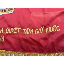 1960s North Vietnam banner embroidered in yellow thread on a red ground, roughly translates as 'Peoples Army of Viet Nam. Warriors of Viet Nam Determined To Keep The Country 1964' around a central military crest with the motto 'Warriors Keep The Country'; tassels to three sides 70 x 100cm