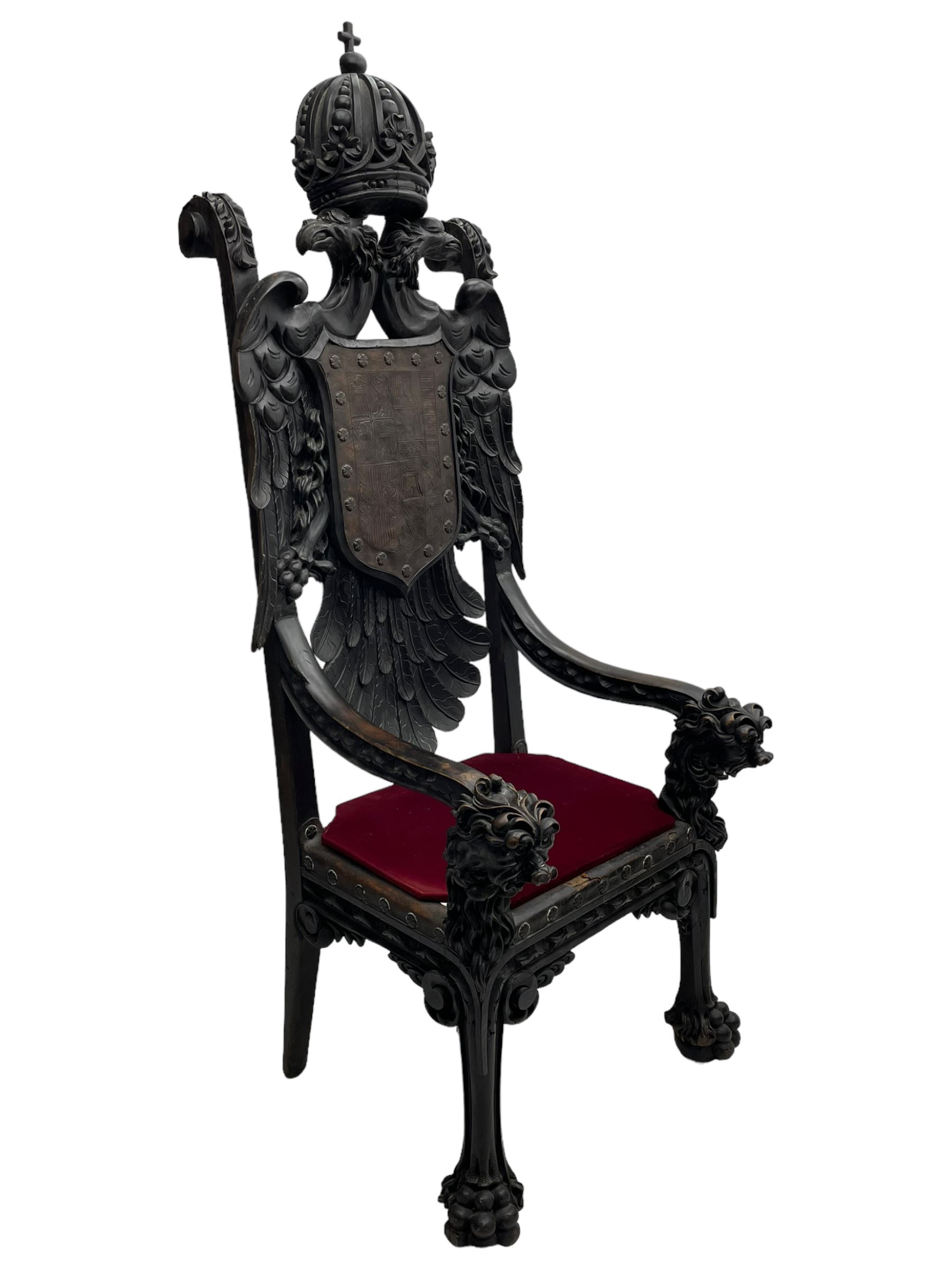 Grand mid-to-late 19th century heavily carved beech framed throne chair, the crown pediment carved with flower heads and cross finial, scroll and acanthus carved upright supports with twin perching griffin back enclosing etched leather work heraldic shield with castle and lion motifs over splayed feathers, flower head carved down sweeping arms with grotesque carved terminals, the seat rails carved with further flower heads on moulded supports with oversized ball and claw carved feet

Provenance: A very similar chair was used in the filming of Stanley Kubrick's 'Eyes Wide Shut' (1999)
