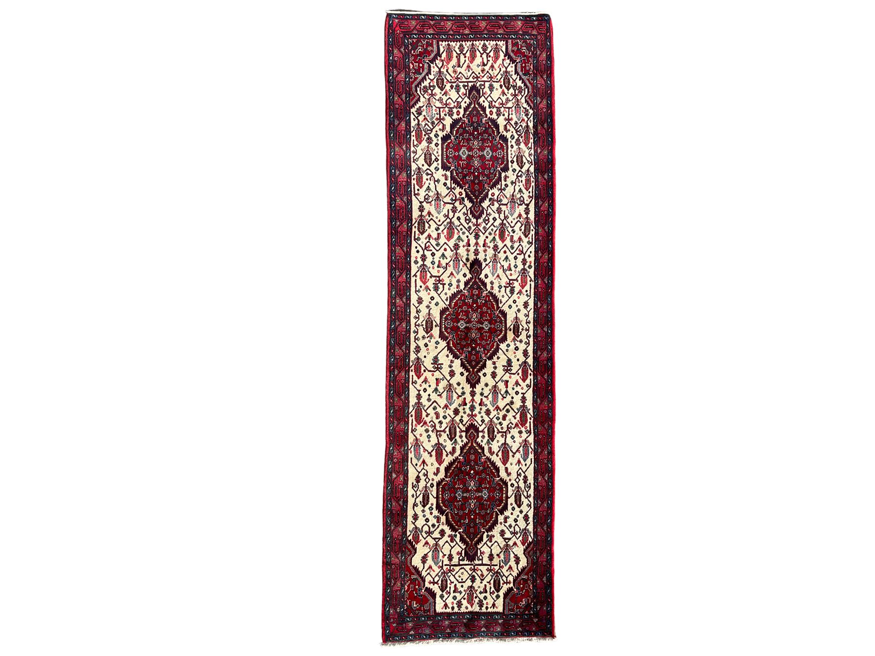 North West Persian Saveh crimson ground runner rug, the three lozenge pole medallions in an ivory field, surrounded by stylised plant motifs, the guarded border decorated with repeating geometric patterns