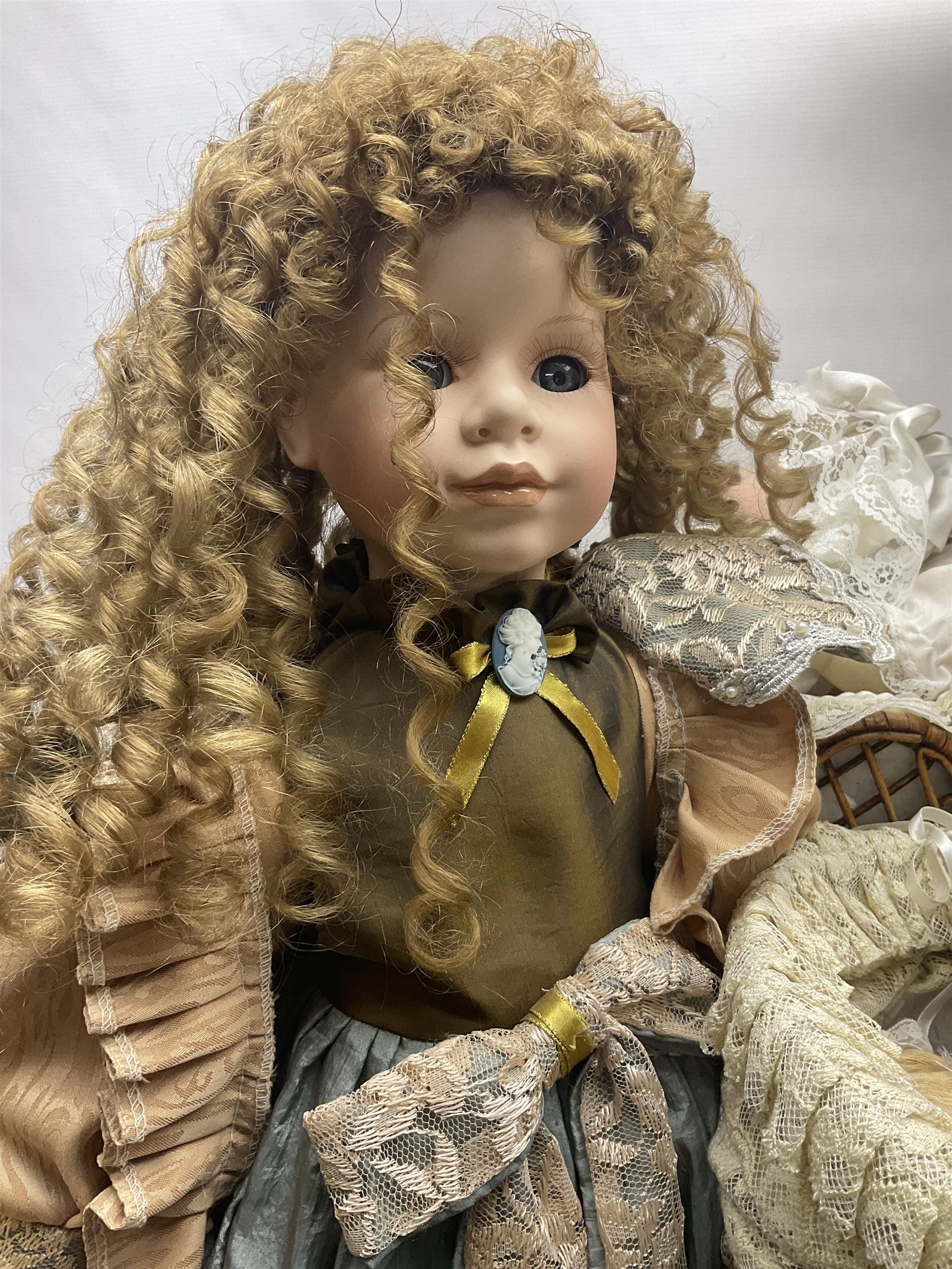 Two decorative wicker dolls prams, one with lace parasol,  and eleven dolls, including Leonardo Collection porcelain dolls, tallest pram including parasol H105cm