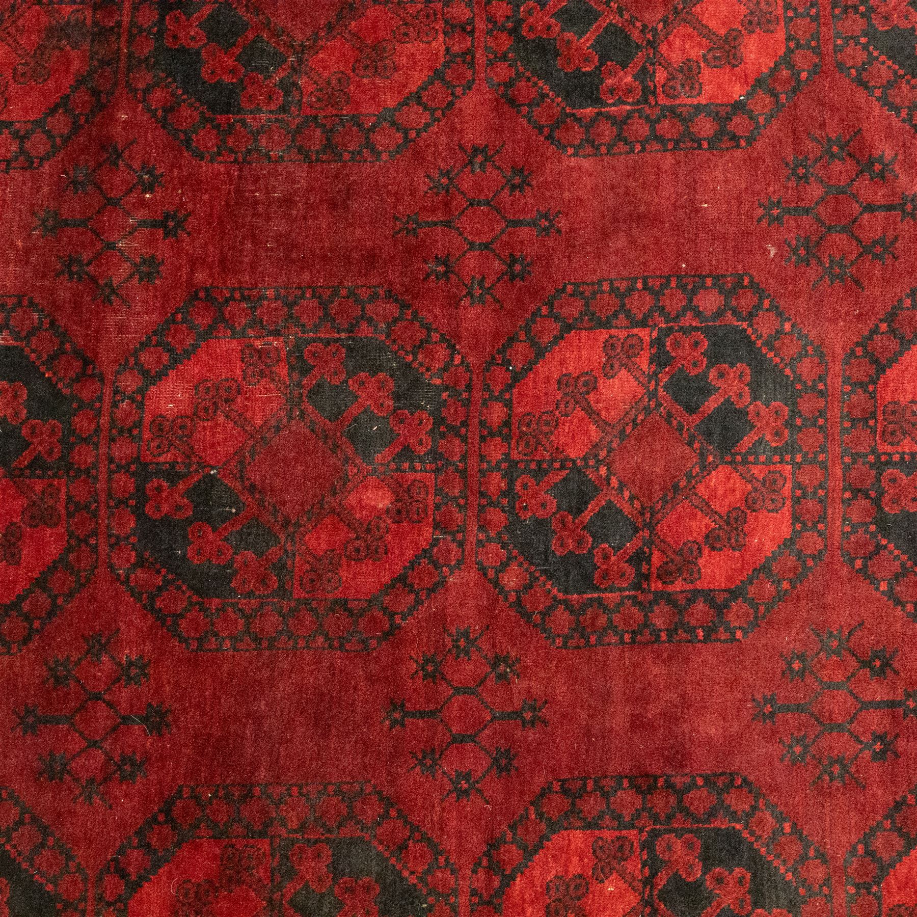 Turkmen Bokhara carpet, with a deep red field and repeating rows of black gul motifs, within multiple geometric borders