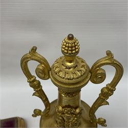 Pair of gilt metal urns, with twin handles, applied cherub detail and stylised pineapple finials, each upon a stepped gilt base, H28cm  
