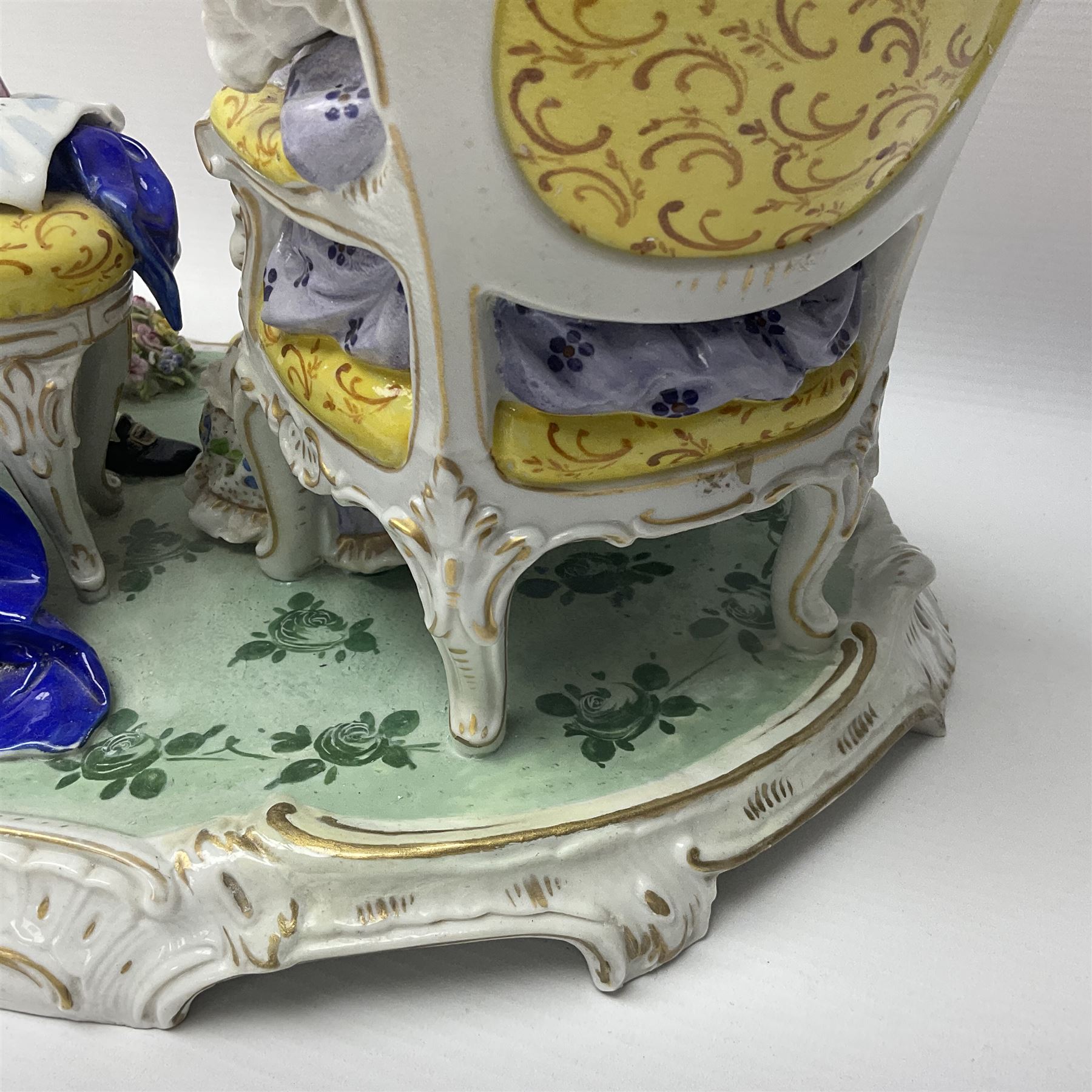 20th century Naples figure group, modelled as a seated female figure playing the lute seated, before a male figure stood holding a sheet of music, each in period dress, upon an oval base with gilt heightened scroll edge, with crowned N mark beneath, H31.5cm L33cm
