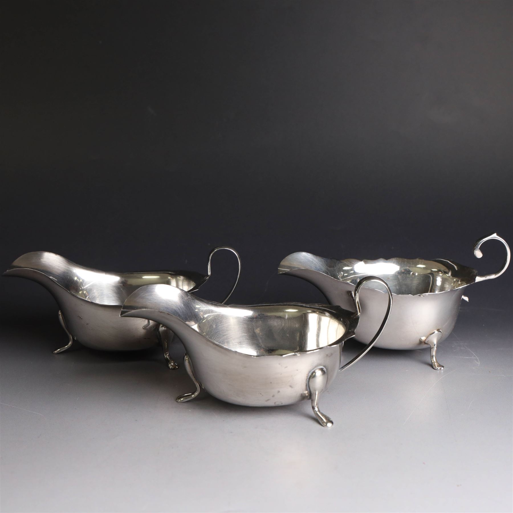 Three silver sauce boats, comprising pair of 1930s silver sauce boats, of typical form with shaped rim, scroll handle and upon three pad feet, hallmarked Viner's Ltd, Sheffield 1932 and a similar 1920s example with flying C scroll handle and upon three paw feet, hallmarked James Deakin & Sons, Sheffield 1923, tallest including handle H7.5cm