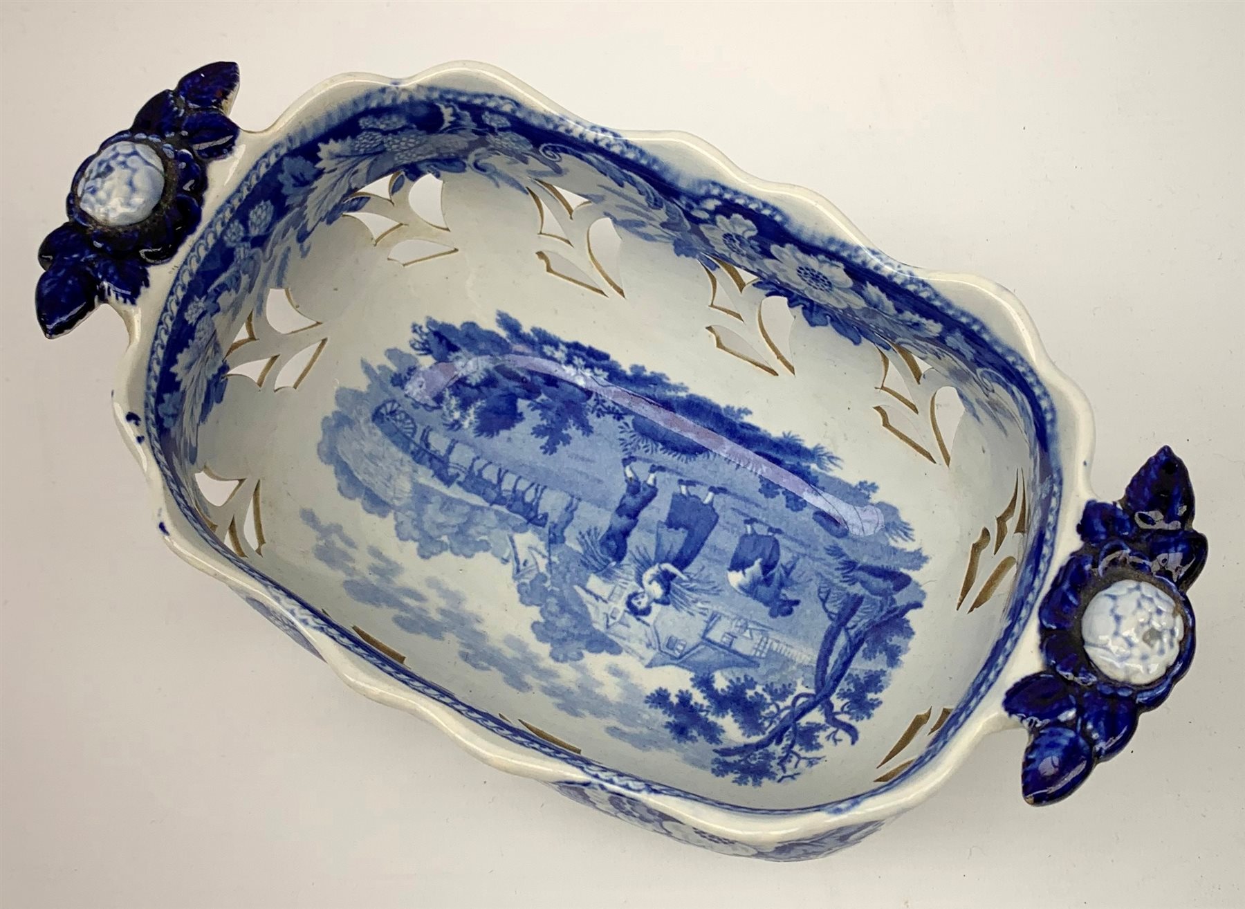 Mid 19th century blue and white transfer printed pearlware reticulated chestnut basket, of oval form with twin handles, decorated to the interior with figures before a classical temple within a garden setting, including handles W26cm, together with a mid 19th century blue and white transfer printed pearlware stand with reticulated edge, decorated with a Willow Pattern, L25cm, and a John and William Ridgeway blue and white transfer printed twin handled pierced basket, decorated with a pastoral scene containing figures at work, with printed mark beneath, including handles L25cm