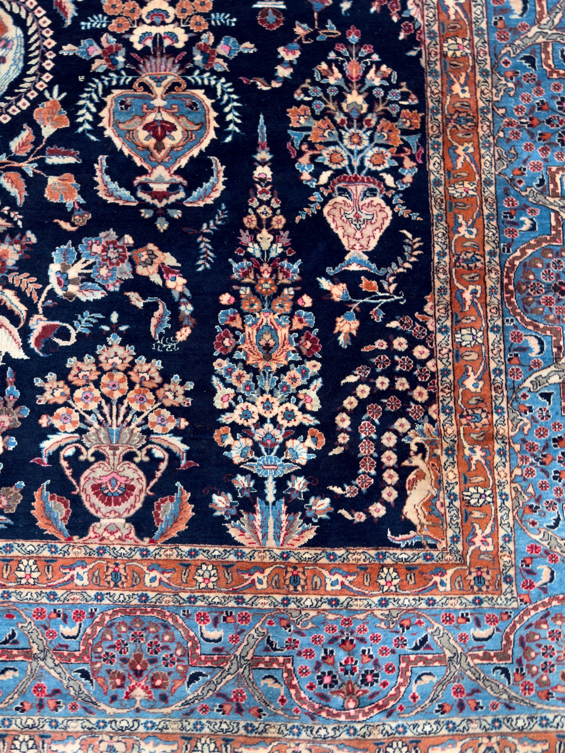 Northeastern Persian Meshed carpet, the deep navy field with a symmetrical floral arrangement of stylised flowerheads, palmettes and scrolling vines issuing from a central urn, enclosed by broad rust and blue borders of floral arabesques and lotus forms, from the region of Meshed