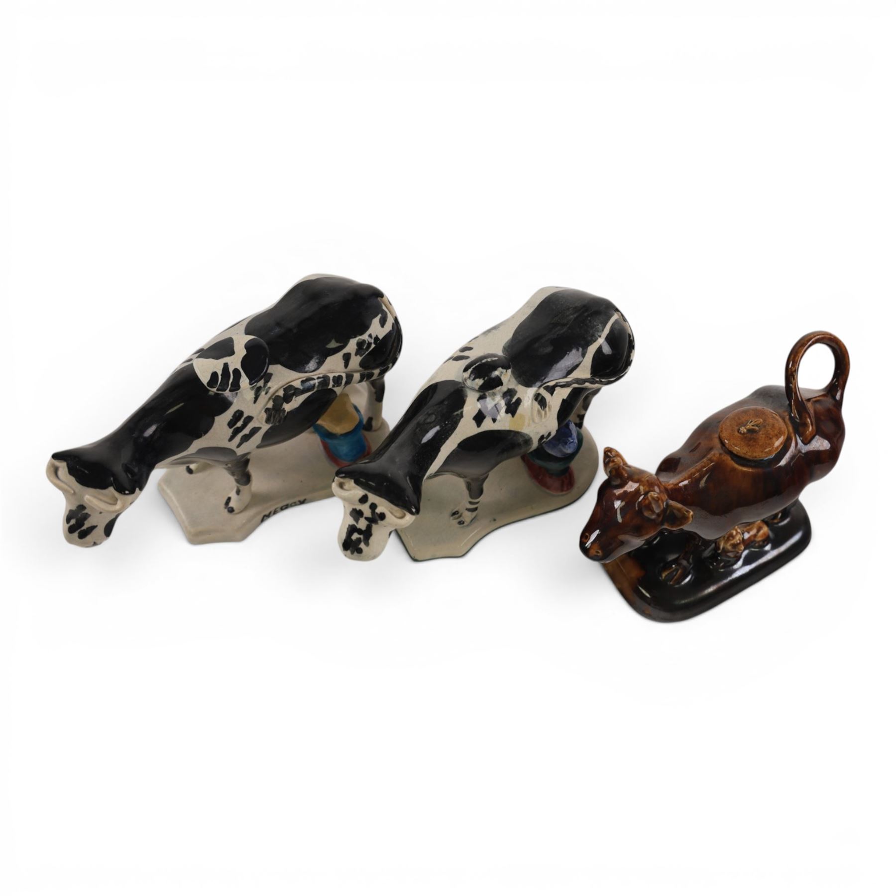 Three Staffordshire cow creamers, one with treacle glaze, the other two painted black and white with a seated figure of a milkmaid, H14cm