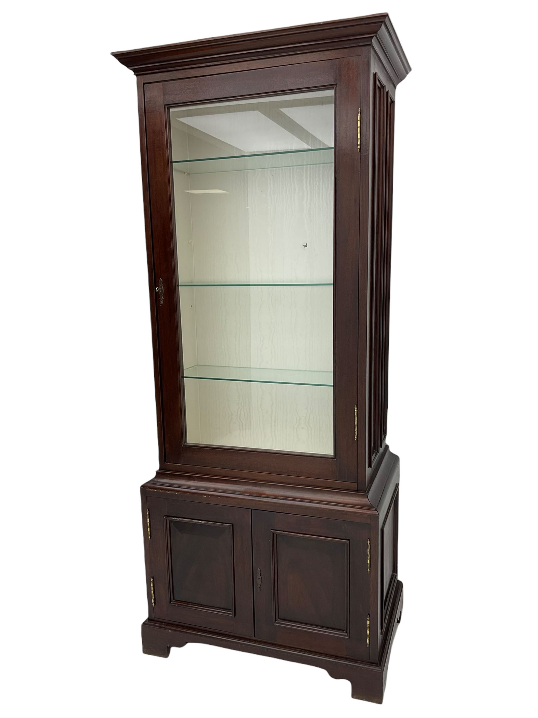 Mahogany display cabinet with hidden compartment, projecting cornice over single glazed door enclosing glass shelves, double panelled cupboard below, the interior with button releasing sliding back compartment, on bracket feet