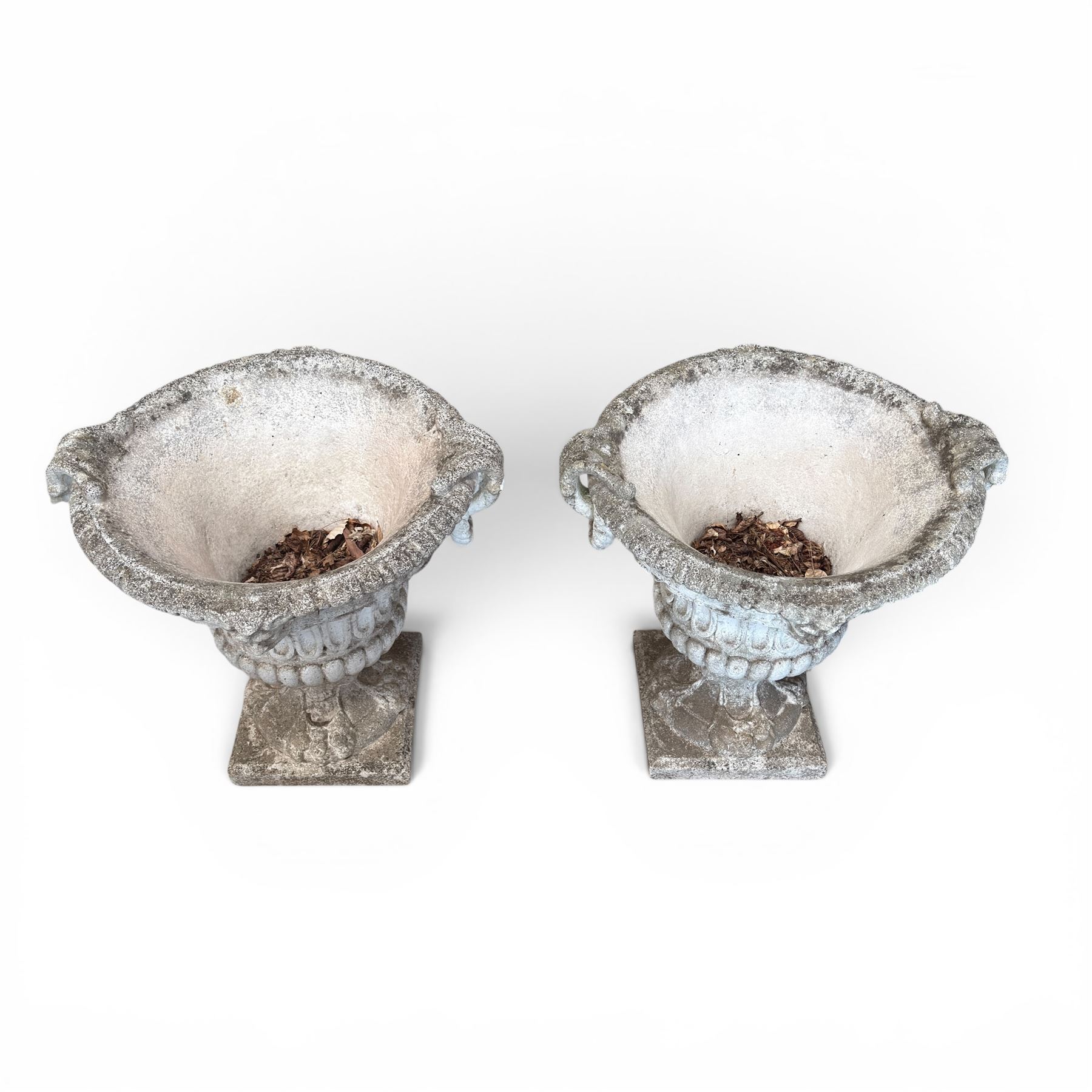 Pair of Neoclassical design cast stone garden urns, each of campana form with fluted body and gadrooned underbelly, decorated with faun/satyr opposing masks and ropetwist handles, with floral and mask design to the socles, raised on square bases, finished in weathered white patina