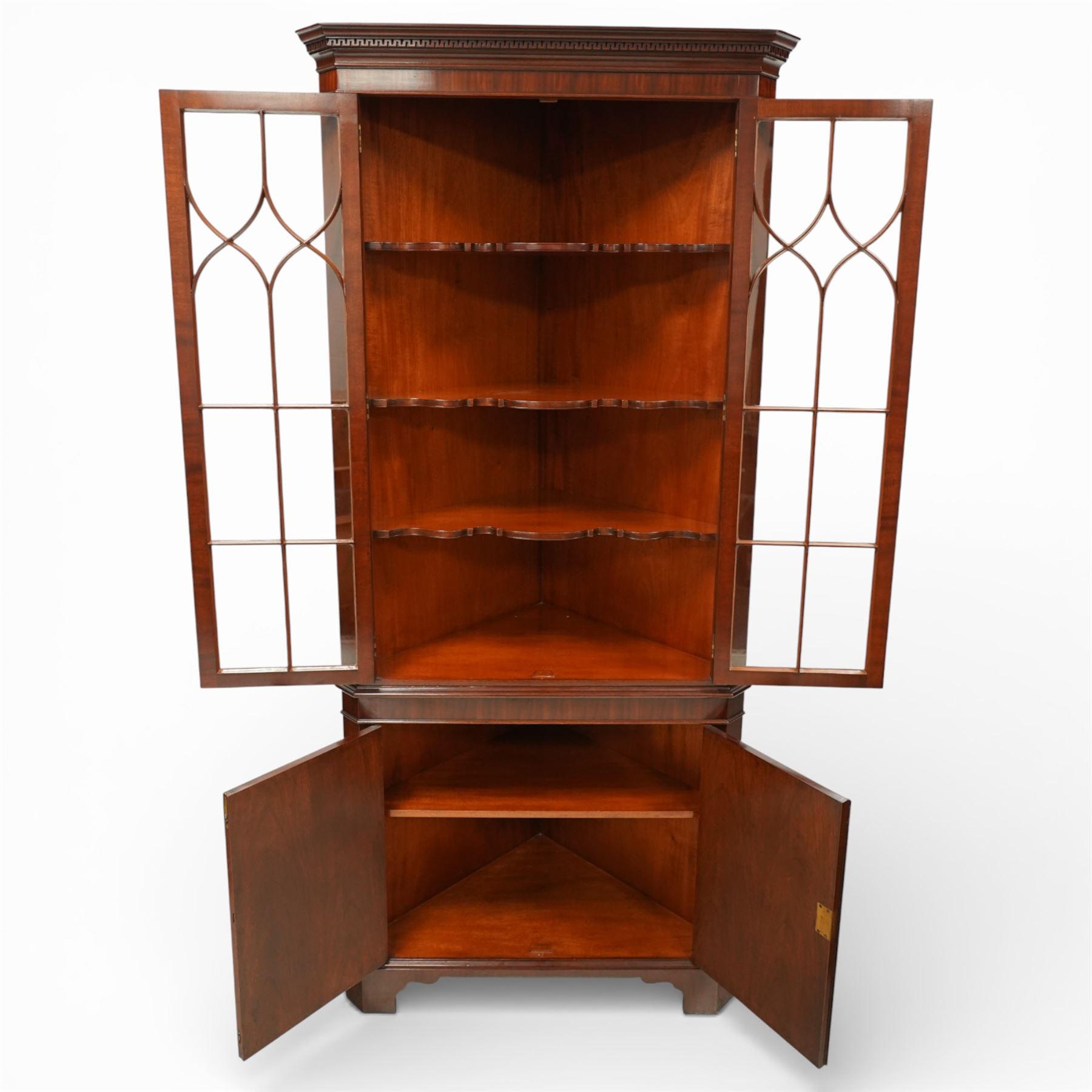 William Tillman - Early 20th century mahogany corner cabinet, the projecting moulded cornice with dentil detail over a glazed upper section enclosed by a pair of astragal glazed doors with Gothic arched tracery, the interior fitted with shaped shelves, above a moulded waist and a lower cupboard enclosed by two panelled doors with shaped fielded panels, raised on bracket feet