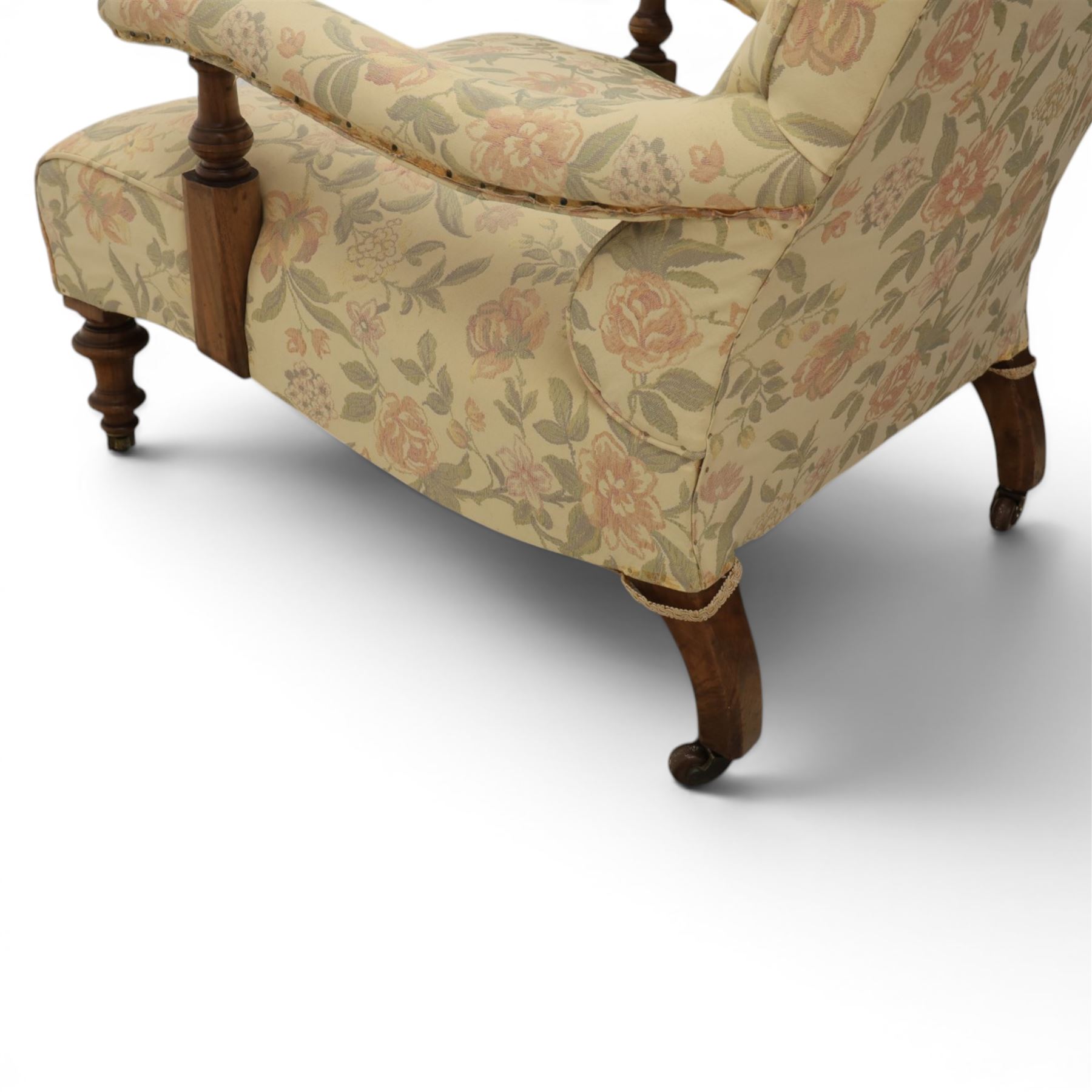 Victorian mahogany framed deep seat low drawing room chair, upholstered in beige floral fabric, on turned supports terminating in castors