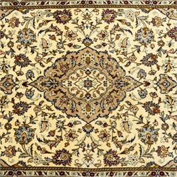 Central Persian Kashan hand-knotted rug, ivory ground, with a central shaped floral medallion with pendants, surrounded by scrolling foliate and floral motifs incorporating rosettes, palmettes and delicate vine work, enclosed by a beige border with repeating palmettes and meandering vines, flanked by narrow floral guard stripes, with cotton fringes