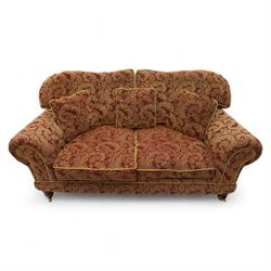 Duresta - two seat settee, upholstered in red and gold damask fabric with piped edges, scroll arms and loose feather-filled cushions, raised on turned wooden feet with brass castors