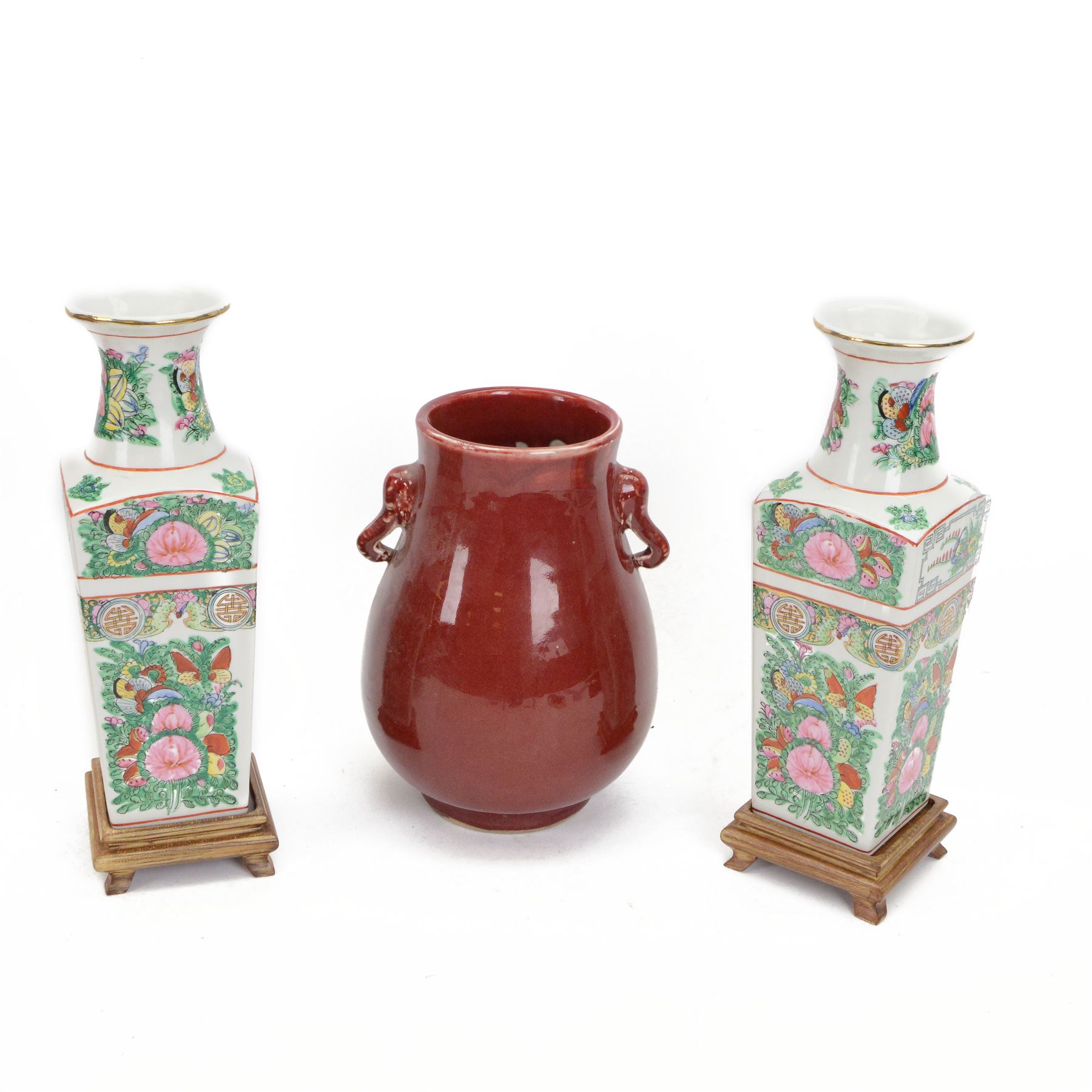 20th century Chinese sang de boeuf vase of baluster form with elephant head handles, togehter with a pair of famille rose vases decorated with floral decoration and insects, upon wooden stands   