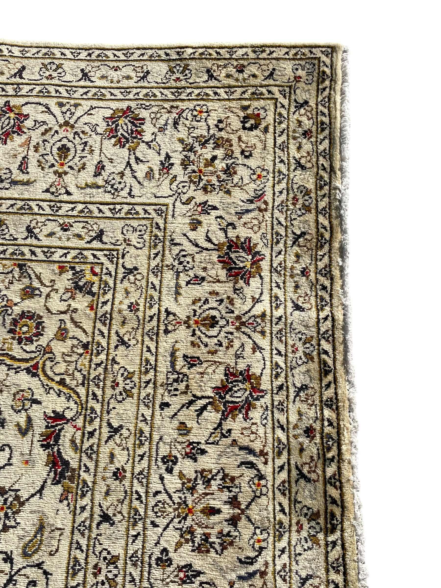 Persian Kashan ivory ground carpet, central medallion decorated with sixteen arranged palmette motifs, within a field decorated with swirling leafy branches and stylised plant motifs, the main border decorated with matching swirling pattern, within floral pattern guard stripes 