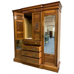 Edwardian walnut combination breakfront triple wardrobe, projecting cornice over cushioned and fluted frieze, central fielded panelled cupboard carved with foliate decoration above two short and three long drawers, flanked by two bevelled mirror doors enclosing hanging hooks with single drawers to base, retailed by J Tonks & Sons, Scarborough