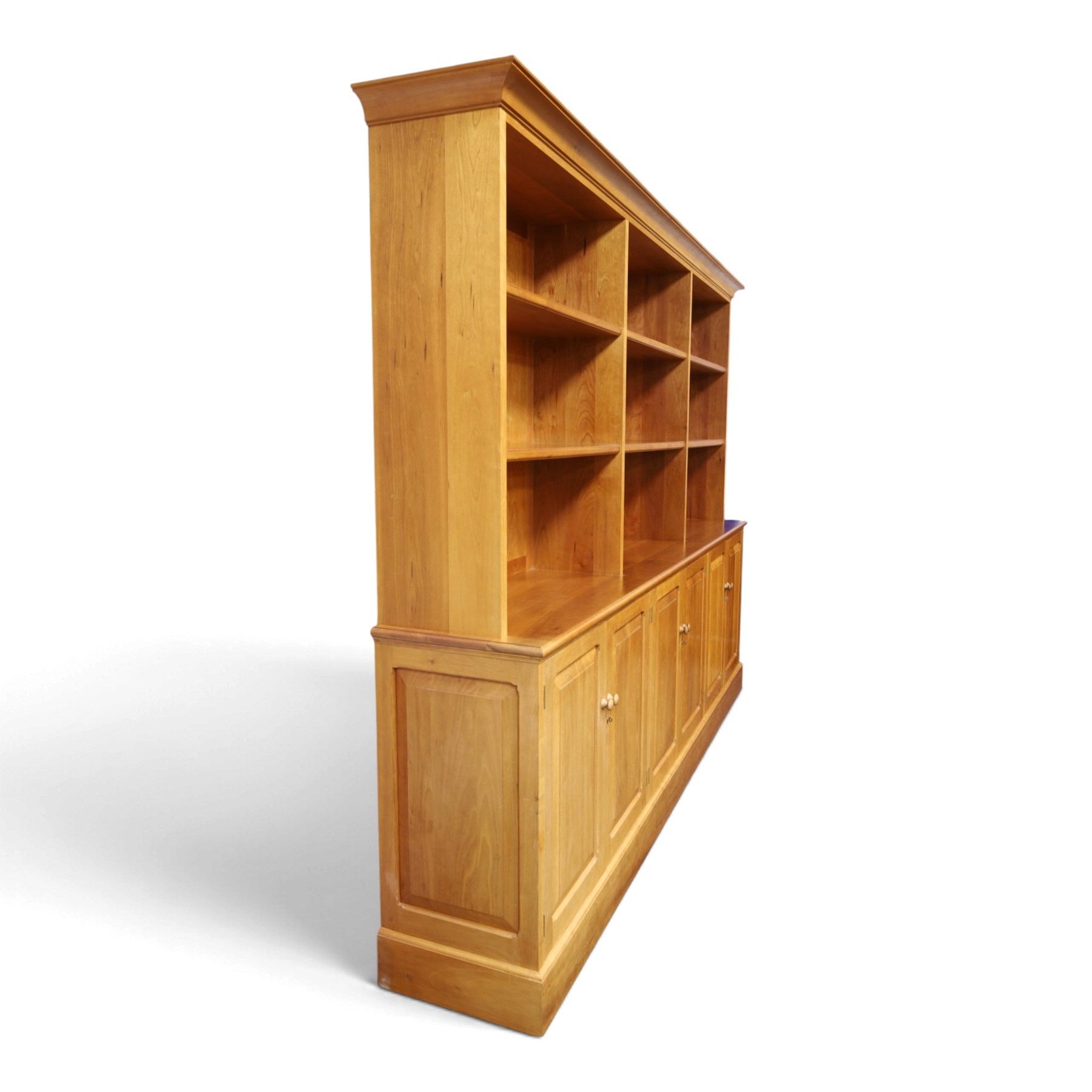 Philip Koomen (1953-) - Craftsman-made modern cherrywood large open
bookcase with a cupboard base, upper section with a
shaped cornice above three sections with two open
shelves, the lower section has three cupboards,
each with two panelled doors enclosing a single
shelf, raised on a plinth base