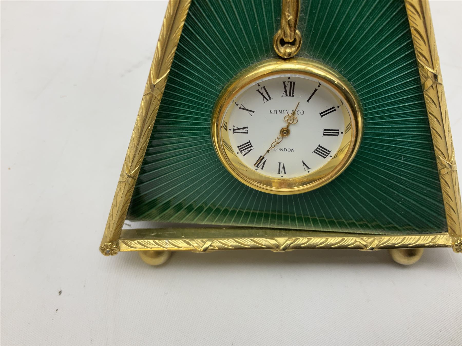 Kitney & Co small desk clock, in green guilloche enamel case of triangular form, decorated with gilt throughout, raised upon two bun feet, H12cm