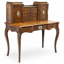 Late 19th-century Louis XV revival gilt bronze mounted and walnut Bonheur-de-Jour, rectangular-shaped serpentine form, with gilt bronze beading, frieze with two blind drawers and gilt bronze handles, centre drawer with large central serves style porcelain plaque, the elevated section with brass gallery above panelled cupboard doors also with serves style porcelain plaques and gilt bronze mounts, interior with single shelf, central section with four drawers each with gilt bronze handles, raised on slender cabriole legs fitted with gilt bronze rococo style masks and sabots