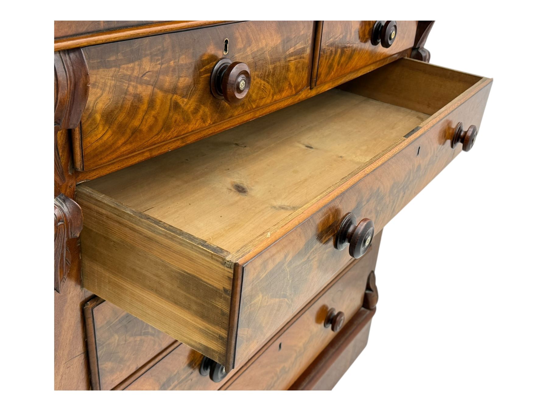 19th century flame mahogany Scotch chest, frieze long drawer above two short and four long graduating drawers, with turned knobs scrolled carved side bracket 