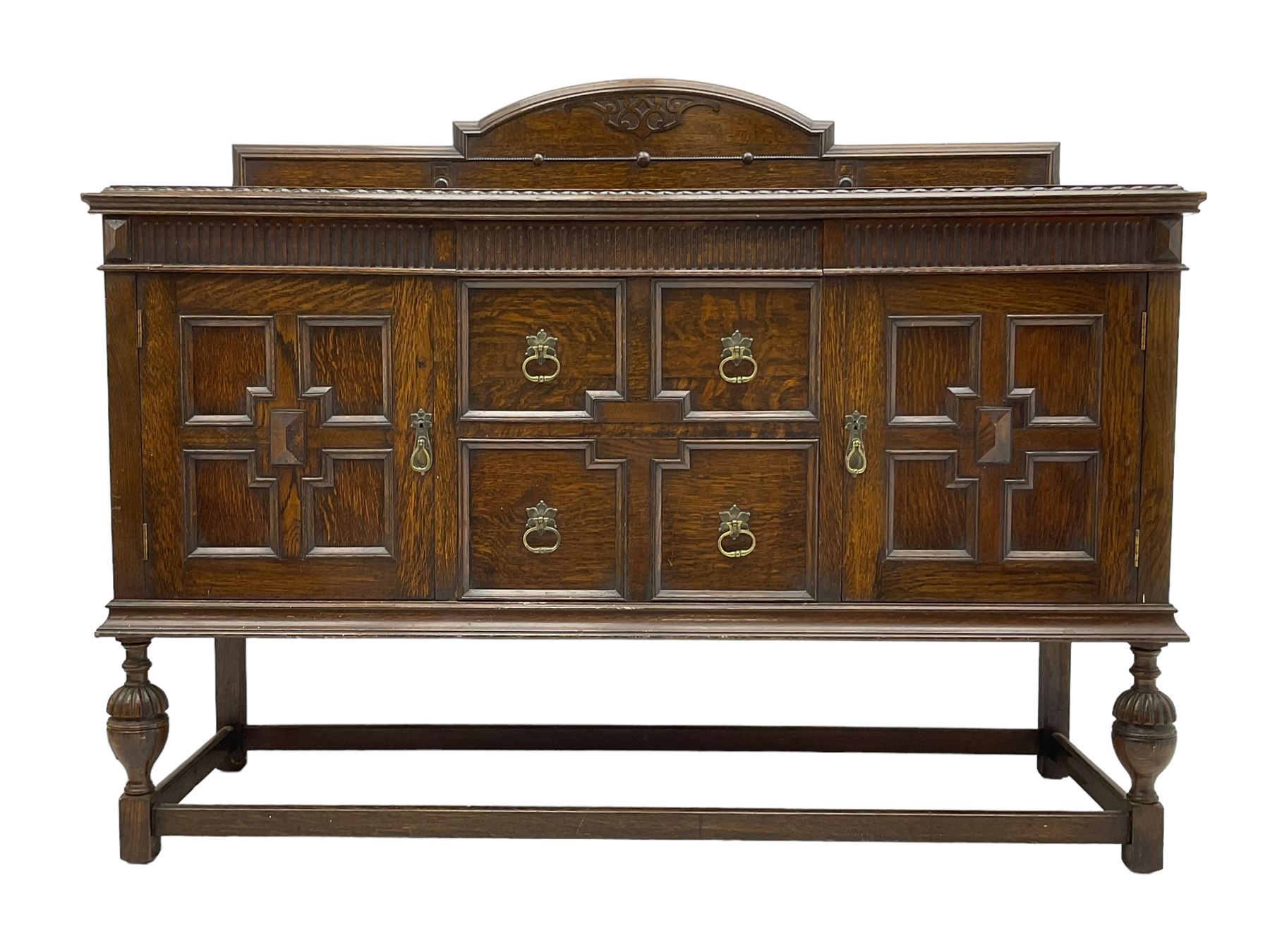 Early 20th century oak sideboard, raised stepped arch back over moulded rectangular top, fitted with two drawers and two panelled cupboards with geometric mouldings, on turned and lobe carved baluster feet united by stretchers 